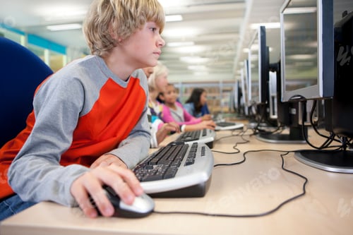 Preview: A Side Profile Shot Of A Young Blonde Boy Using A Mouse On A Computer In A School Computer Lab.