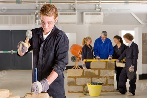Preview: A Young Student In Blue Uniform Hammering Chisel On A Brick In Vocational School While His Teacher