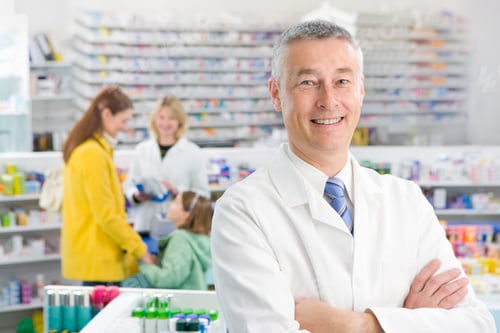 Preview: A Smiling Pharmacist Standing With His Hands Crossed And Looking At Camera In A Pharmacy Store With