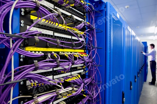 Preview: A Close Up Shot Of Lan Cables And Blue Network Servers With A Man Standing In Background.