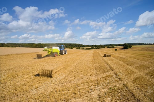 Preview: A Wide Shot Of Blue Tractor And Straw Baler Stacking Straw In A Sunny Rural Field.