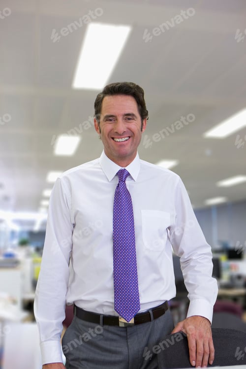 Preview: A Vertical Portrait Of A Smiling Businessman Standing Next To A Chair In The Office