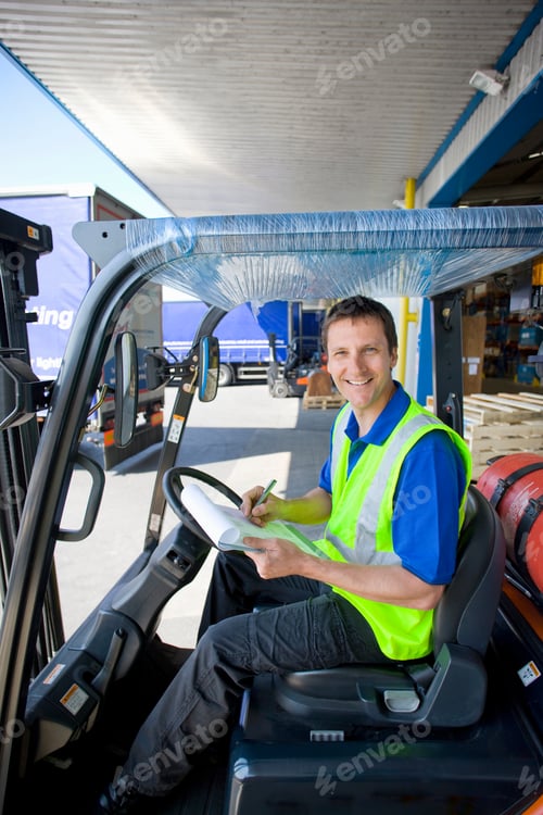 Preview: A Worker In The Driver Seat Of A Forklift Smiling At The Camera At A Loading Dock Holding A Pen And