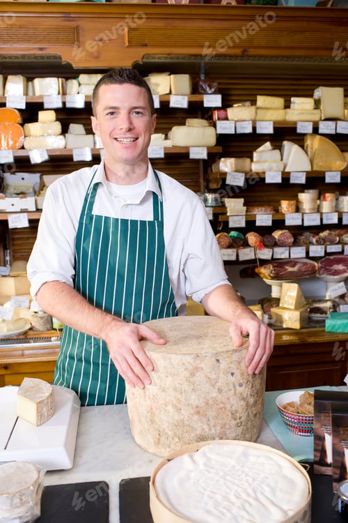 Preview: A Portrait Shot Of A Smiling Salesman Holding A Big Cheese Slab And Standing At A Counter In A