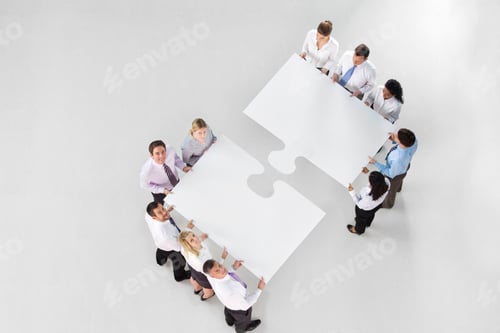 Preview: Overhead Shot Of Two Groups Of Businesspeople Holding A Large Jigsaw Piece Coming Together To Merge