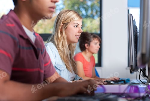 Preview: A Young Blonde Woman Looking At A Computer In A Computer Lab With Other Students In Background.