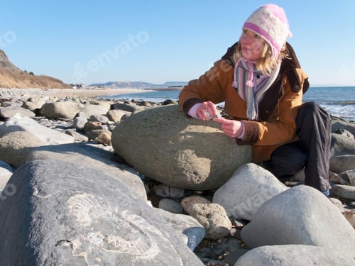 Preview: A Medium Shot Of A Blonde Woman Looking Up While Holding A Rock On Ocean Beach In Winter.