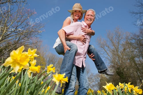 Preview: Low Angle Shot Of A Joyous Senior Couple Piggybacking In A Daffodil Field On A Sunny Day Smiles At