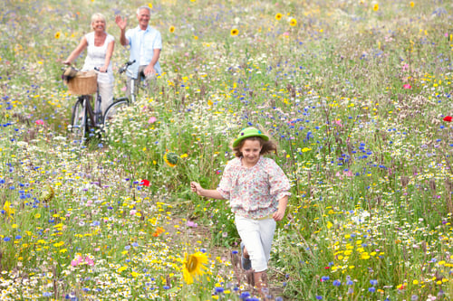 Preview: A Medium Shot Of A Young Girl Wearing A Hat Running In A Wildflowers Field With A Senior Couple