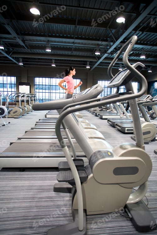 Preview: A Vertical Wide Shot Of A Young Woman Running On A Treadmill In A Gym.