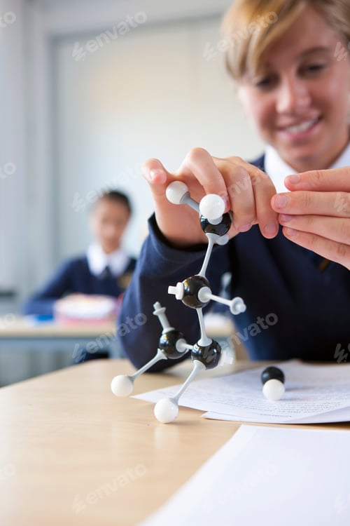 Preview: A Portrait Close Up Shot Of A Young Blonde Girl In School Uniform Assembling An Atom Model On Her