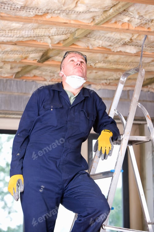 Preview: A Portrait Shot Of A Man In Coveralls Casually Standing On A Ladder And Looking Up.