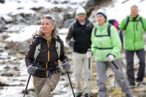 Preview: Senior Couples Carrying A Backpack And Trekking Poles While Crossing A Stream In The Snowy Woods
