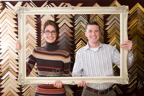 Preview: A Smiling Couple Holding A Golden Frame And Looking At The Camera Through It.