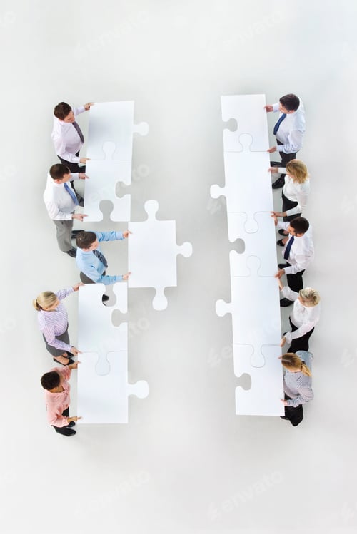 Preview: High Angle Shot Of A Group Of Businesspeople With Large Jigsaw Pieces In Two Rows Standing Face To