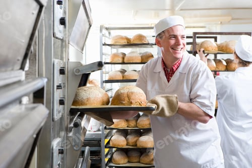 Preview: A Medium Shot Of A Young Baker Smiling And Looking Behind While Removing Fresh Loaves Of Bread From