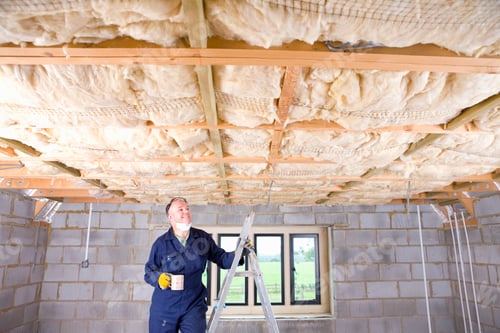 Preview: A Man In Coveralls Drinking Coffee On A Ladder And Looking Up At Ceiling Insulation In An Attic.