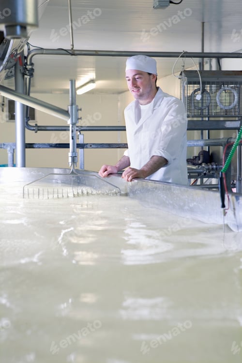 Preview: A Portrait Shot Of A Cheese Maker Wearing A Coat Watching Closely In A Vat Machine While Rennet And