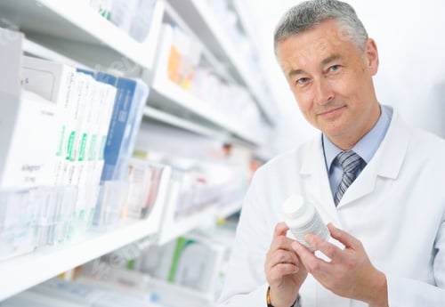 Preview: A Close Up Shot Of A Pharmacist Holding Medicine Bottles While Looking At The Camera.