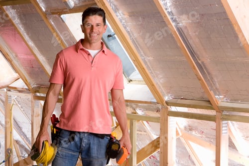Preview: An Electrician Looking At The Camera And Smiling In An Under Construction Attic.