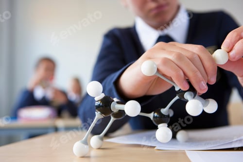 Preview: A Close Up Shot Of A Student'S Hand In School Uniform Assembling An Atom Model At A Desk.