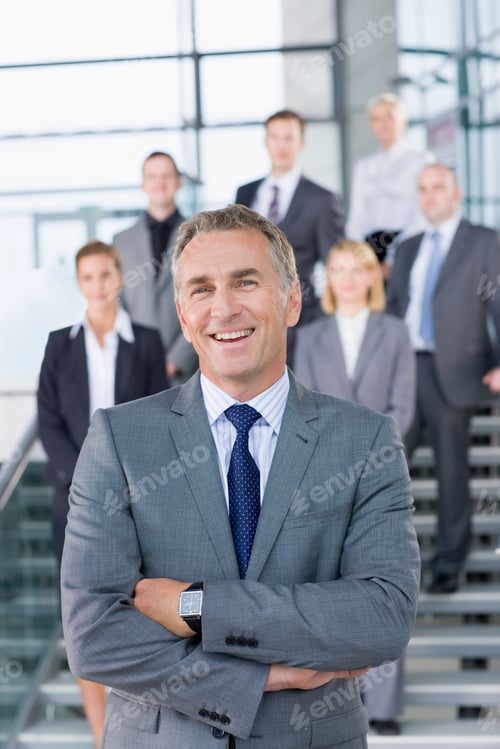 Preview: Portrait Of A Smiling Businessman Having His Arms Crossed In A Formal Suit With Colleagues Standing