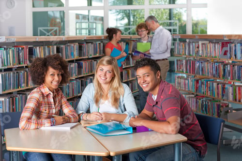 Preview: A Medium Shot Of Young Students Smiling At Camera While Studying In A School Library With Teacher