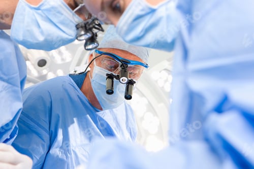 Preview: A Senior Surgeon In Selective Focus Looks Down At The Operation Table The Surgical Loupe During A
