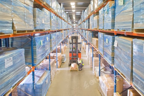 Preview: A High Angle Wide Shot Of A Female Warehouse Worker Sitting Down And Inspecting A Box On A Forklift.