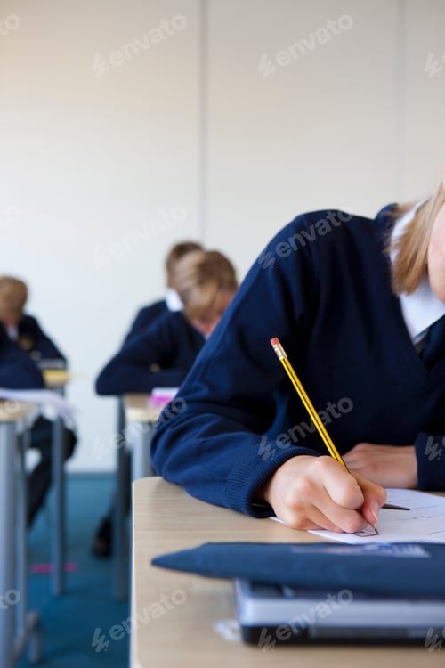 Preview: A Vertical Close Up Shot Of A Young Girl'S Hand In School Uniform Writing A Test At Her Desk In A
