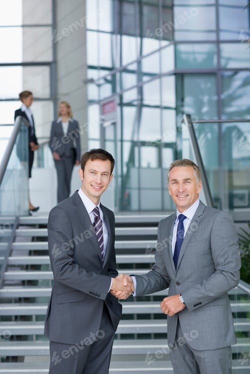 Preview: A Portrait Of Smiling Businessmen In Formal Suits Shaking Hands While Standing Next To A Staircase
