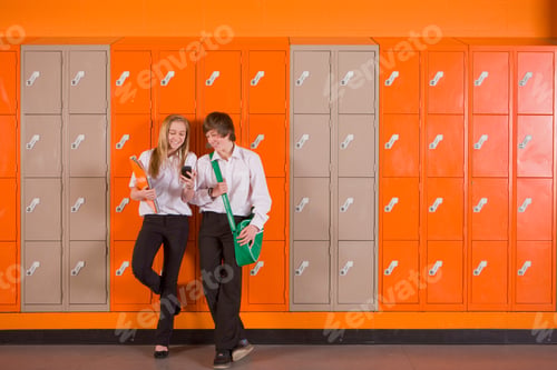 Preview: A Wide Shot Of A Young Boy And A Girl Leaning On School Locker And Looking At A Cell Phone.
