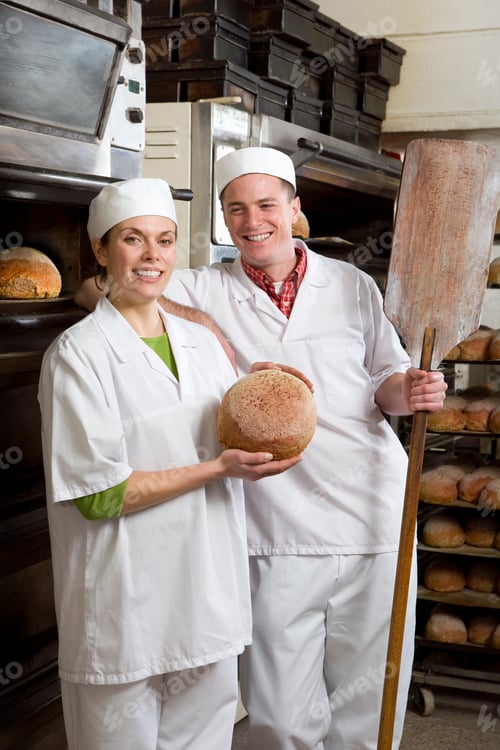 Preview: A Portrait Shot Of A Two Happy Bakers Standing Next To An Oven With A Peel And A Loaf Of Bread In