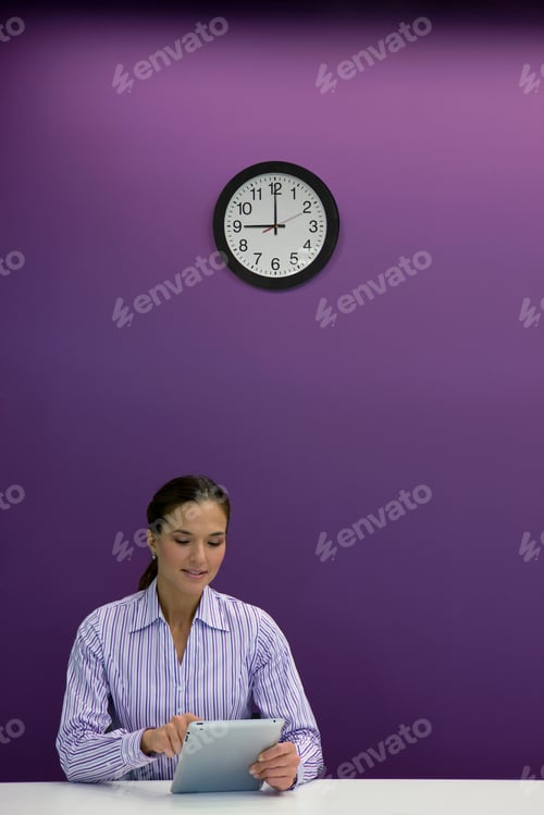 Preview: A Portrait Shot Of A Businesswoman Using Tablet At Her Desk Under A Clock.