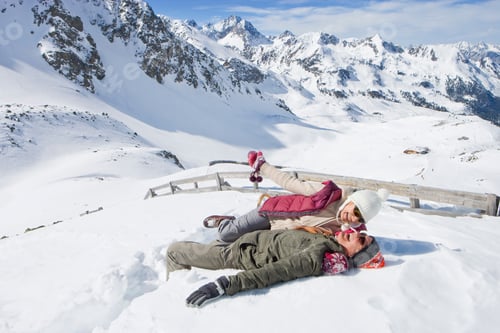 Preview: A Wide View Of A Laughing Senior Couple Lying In The Snow On Top Of A Mountain