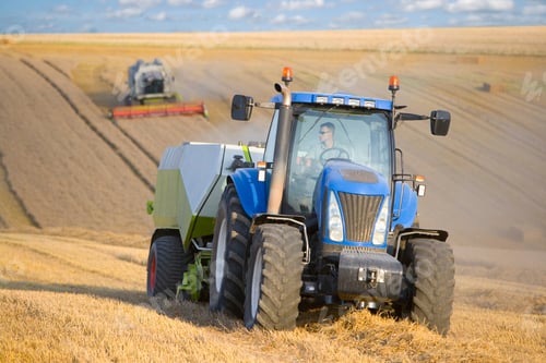 Preview: A Farmer Driving A Blue Tractor Attached To A Straw Baler In A Wheat Field.