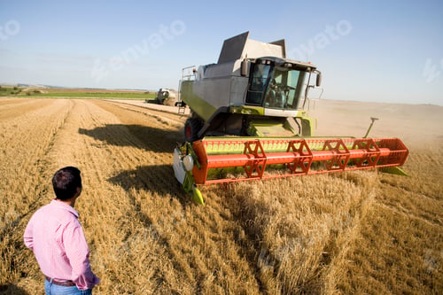 Preview: A Shot Of A Farmer From The Rear Looking At A Combine Harvester In A Barley Field.