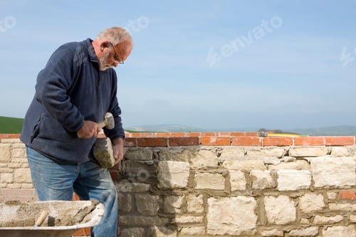 Preview: A Stonemason Chipping Stone With Mallet Next To A Wall.