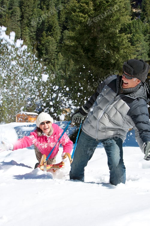 Preview: A Senior-Adult Man Playfully Pulling His Cheerful Wife Through The Snowy Woods While She Is Sitting