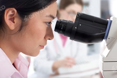 Preview: A Side Profile Close Up Shot Of A Young Female Technician Looking Into A Microscope In A Laboratory.