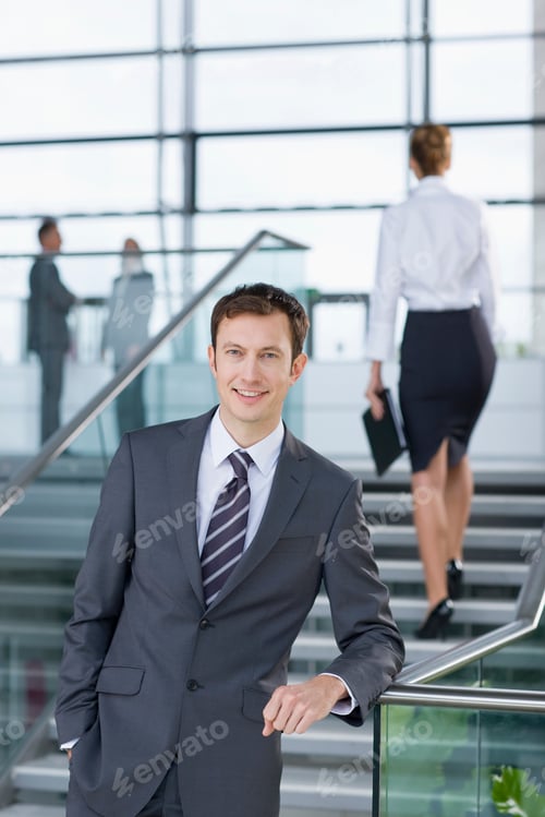 Visualização: Um retrato vertical de um empresário confiante em terno formal, apoiado na grade de um saguão