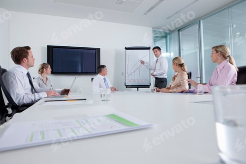 Preview: A Wide View Of A Conference Room With A Smart Businessman Leading A Meeting While Pointing At The