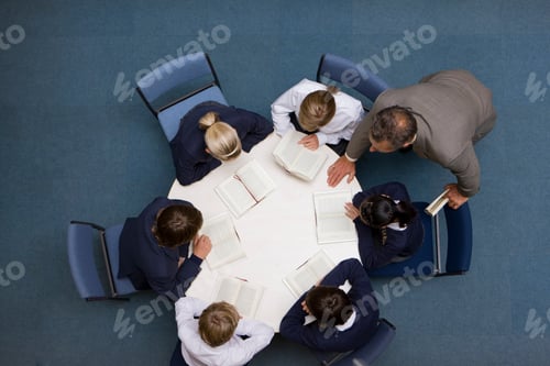 Preview: A High Angle Shot Of A Teacher Guiding His Students While They Are Reading Books At A Round Table.