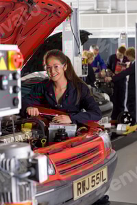 Preview: A Vertical View Of A Young Girl In Mechanic Uniform And Safety Glasses Repairing A Car In The