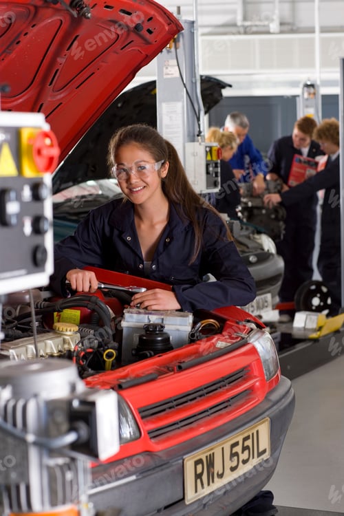 Preview: A Vertical View Of A Young Girl In Mechanic Uniform And Safety Glasses Repairing A Car In The