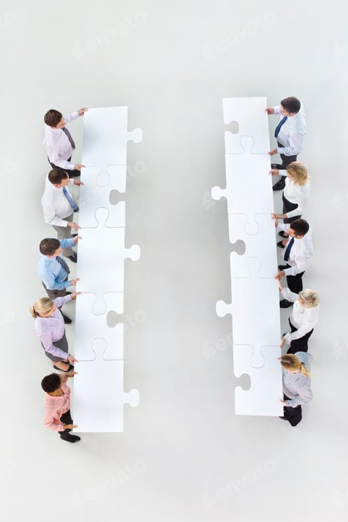 Preview: Vertical Overhead Shot Of A Group Of Businesspeople With Large Jigsaw Pieces In Two Rows Standing