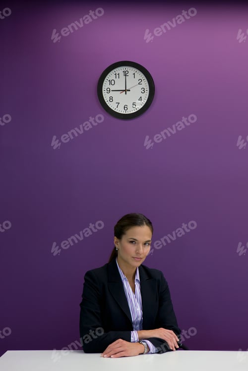 Preview: A Portrait Shot Of A Serious Businesswoman Sitting At A Desk Under A Clock And Looking At Camera.