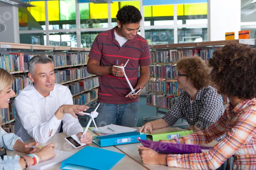 Preview: A Medium Shot Of A Teacher Explaining Wind Turbine Models To His Students Sitting Around A Desk In