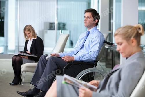 Preview: A Businessman Sitting In A Wheelchair With A Magazine While Waiting In A Lobby Along With Couple Of