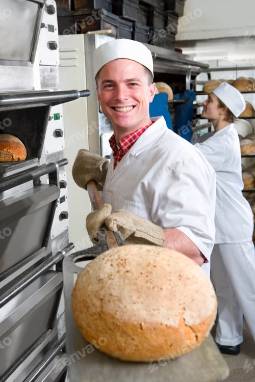 Preview: A Portrait Shot Of A Smiling Baker Showing Fresh Bread To The Camera As He Removes It From Oven.